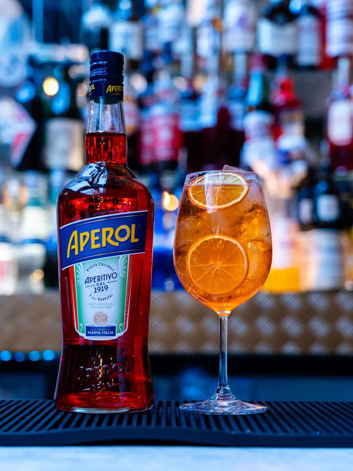Aperol Spritz mit getrockneter Orangenscheibe vor einer Bar-Rückwand
